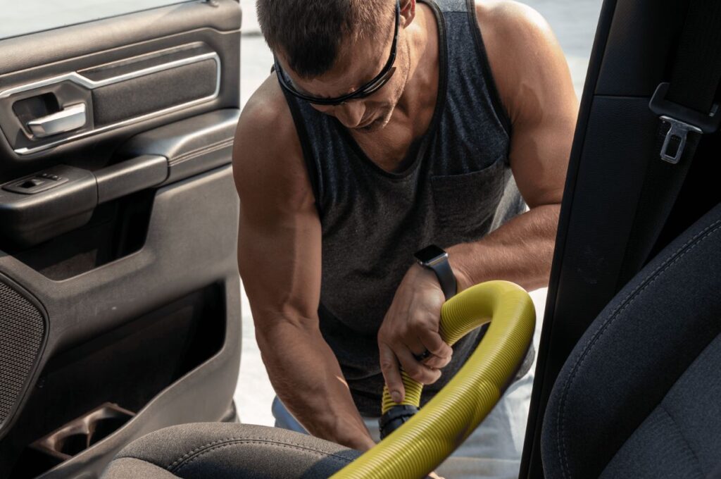 Man vacuuming car interior with yellow hose