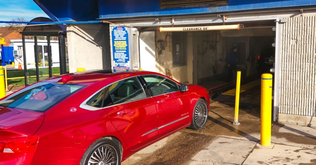 Red car entering automatic car wash tunnel entrance