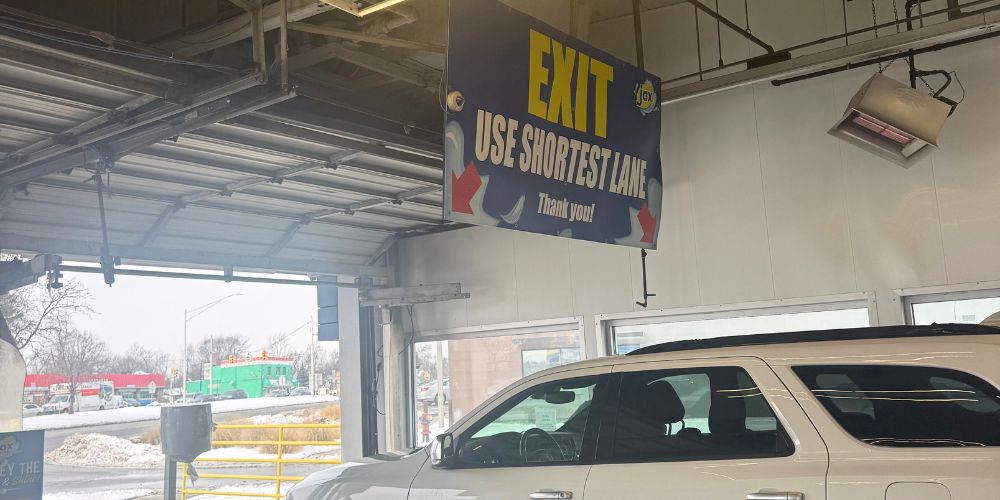 Car exiting wash tunnel under exit direction sign.