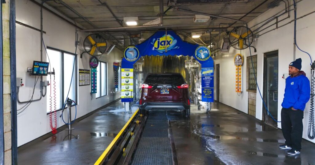Car entering wash tunnel with staff member observing.