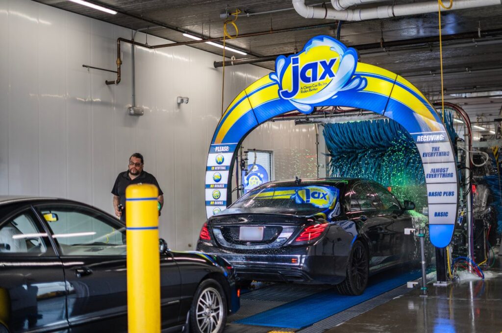 Black luxury car enters automated car wash tunnel.