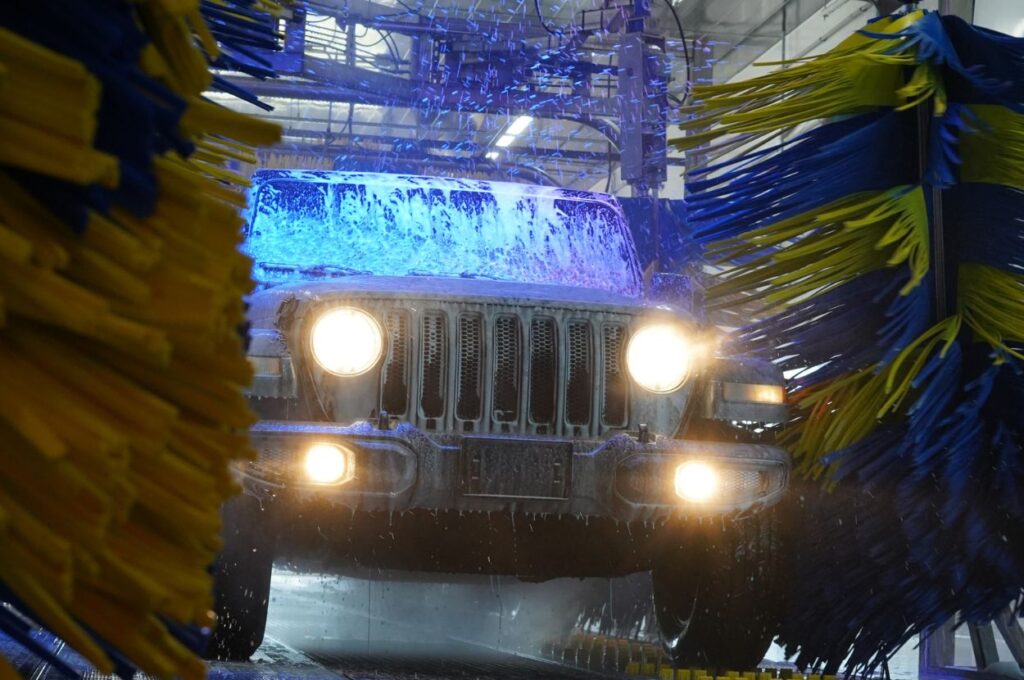 Jeep Wrangler gets washed by large rotating brushes.