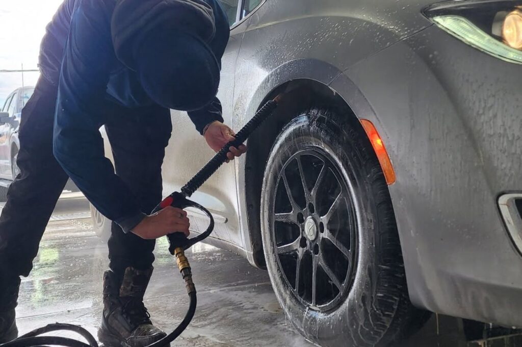 Technician uses high pressure spray on car wheel.
