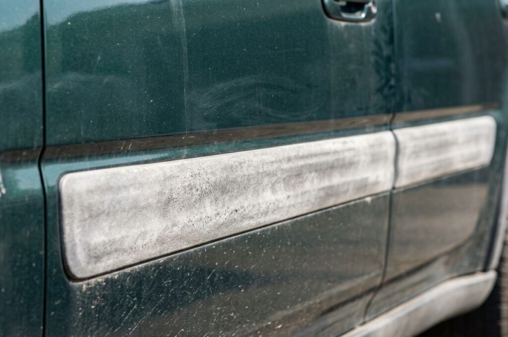 Side view detail of car exterior plastic trim showing fading, chalky oxidation, and color mismatch compared to painted surface