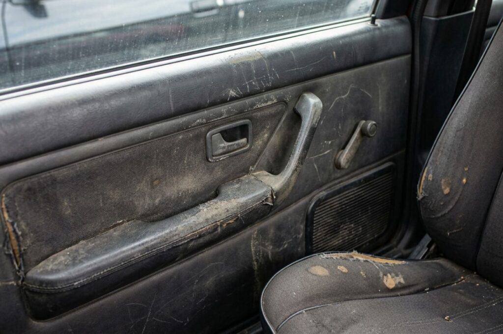 Interior car shot showing worn door panel with light scuffs, faded trim, and minor stains on upholstery