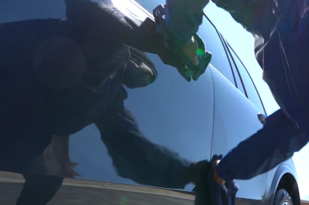 Technician uses blue towel to clean car door.