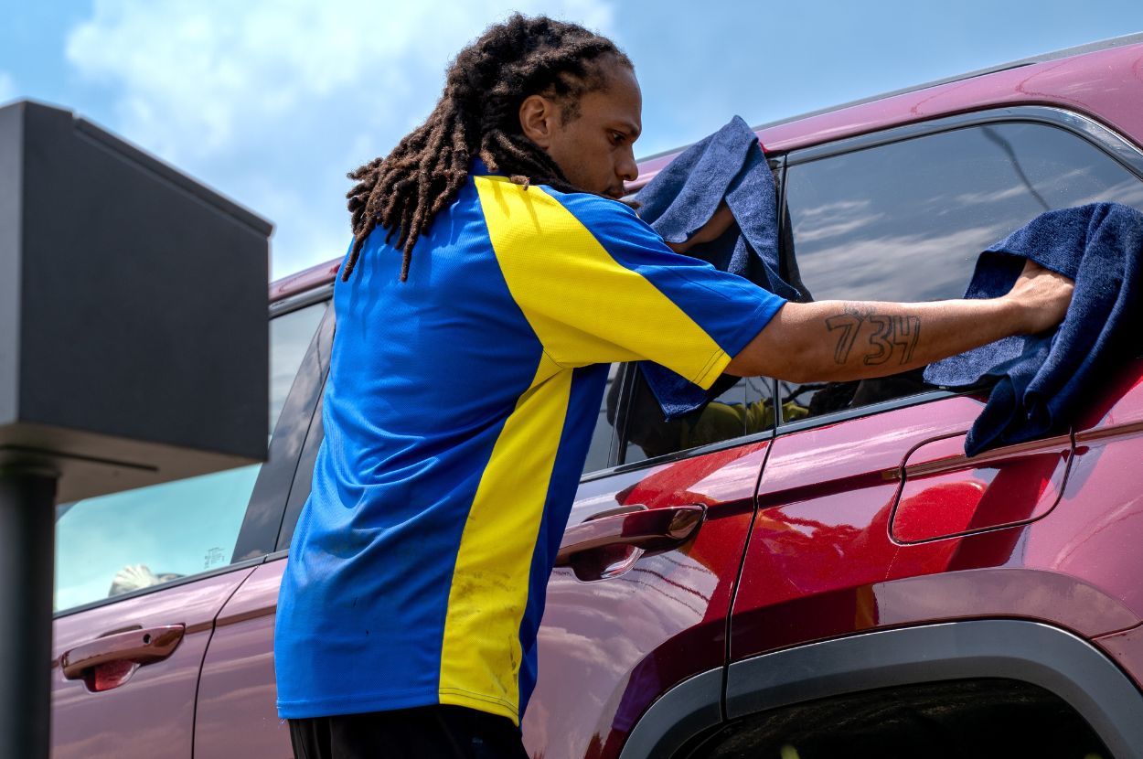 Technician uses blue towels to clean vehicle windows.