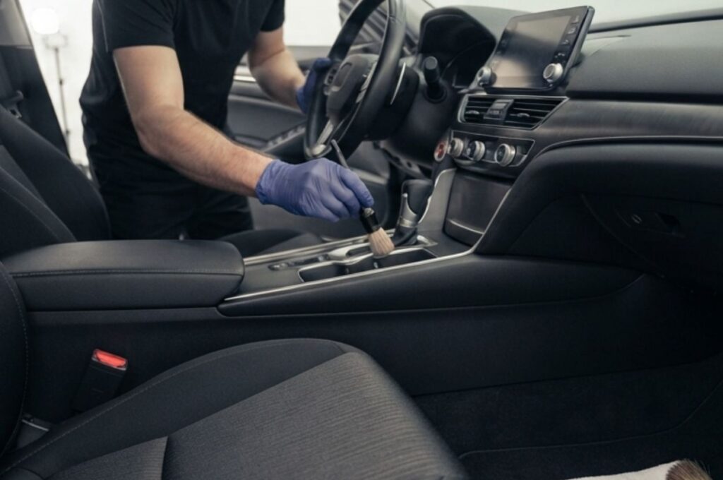 professional detailer carefully cleaning the cloth seats, floor mats, and center console inside a modern sedan