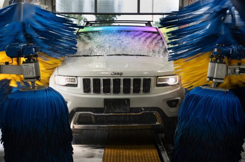 White Jeep inside an automatic car wash with spinning brushes.